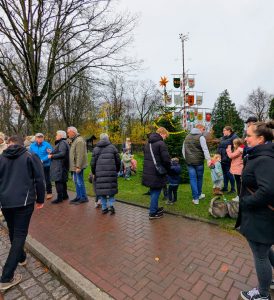 enschen in Winterkleidung stehen und unterhalten sich auf einem Gehweg vor einem geschmückten Weihnachtsbaum mit Wappenbaum im Hintergrund.